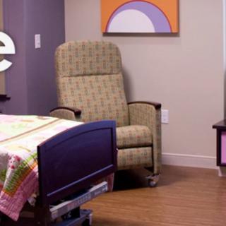 A hospital room featuring a comfortable recliner chair and a bed with colorful blankets.
