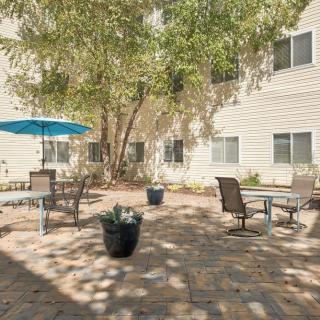 A serene courtyard with outdoor seating and tables under a blue umbrella, surrounded by trees.