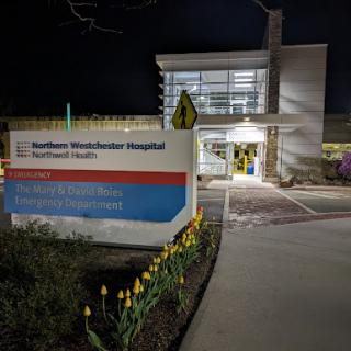 A view of the hospital entrance at night, showcasing modern architecture and illuminated signage.