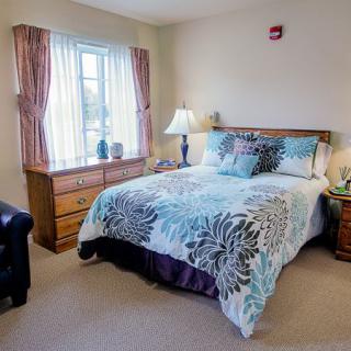 A cozy bedroom with a neatly made bed, wooden furniture, and a window with curtains.