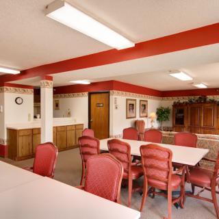 A spacious meeting room with red chairs and white tables, decorated with paintings and plants.