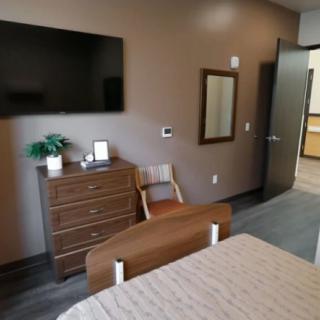 A hospital room with a bed, television, dresser, chair, and mirror.