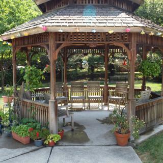 A wooden gazebo surrounded by potted plants in a garden setting.