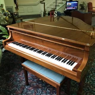 A wooden grand piano with a matching bench indoors.