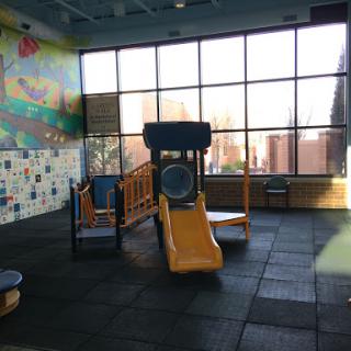 A bright and inviting indoor playground featuring a slide and play equipment, surrounded by large windows.