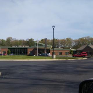 A view of a school building with a well-maintained parking lot and surrounding greenery.
