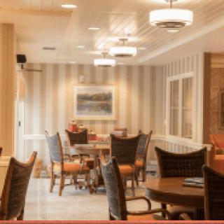 A cozy dining area with neatly arranged tables and chairs, illuminated by elegant ceiling lights.