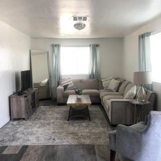 A cozy living room featuring a sectional sofa, a coffee table, a television, and decor elements like curtains and artwork.