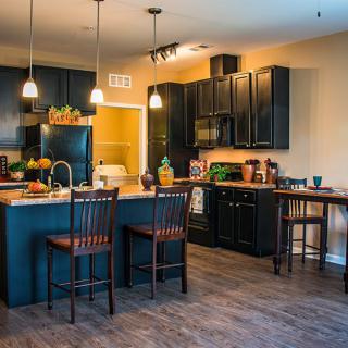 A modern kitchen with black cabinets and a central island, featuring pendant lighting and bar stools.