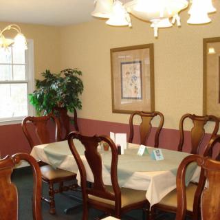 A cozy dining room featuring a large table with wooden chairs, elegant lighting, wall art, and a potted plant near the window.