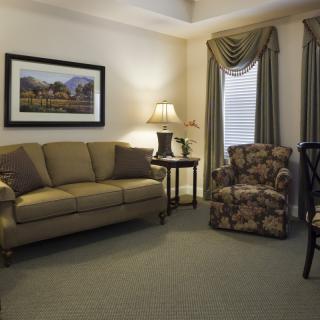 A cozy living room with traditional decor, featuring a beige sofa, floral armchair, and elegant curtains.
