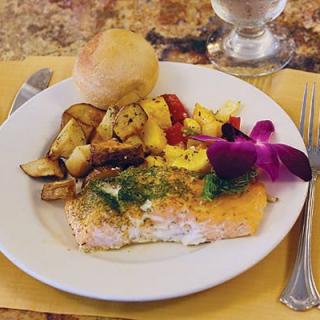 A delicious meal featuring salmon, roasted vegetables, and a roll on a elegantly set table.