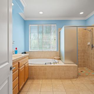 A spacious bathroom with blue walls, featuring a bathtub, shower, and wooden vanity.