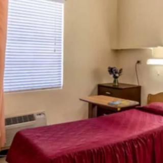 A simple bedroom with a single bed, window blinds, and a small nightstand.