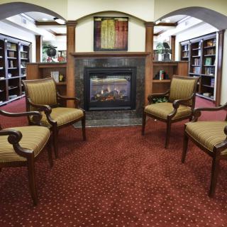 A cozy library seating area with four chairs surrounding a fireplace.