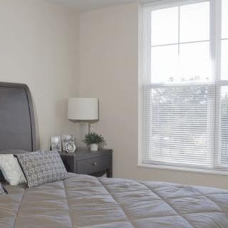 A minimalist bedroom with a neatly made bed, bedside table, and a large window.