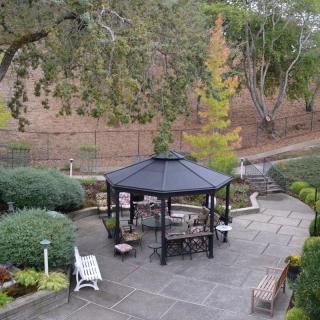 A tranquil garden scene with a gazebo surrounded by lush greenery and seating areas.