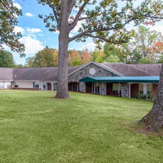 A scenic view of a building surrounded by a lush green lawn and tall trees under a clear sky.