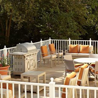 A cozy outdoor patio with seating and a grill, surrounded by lush greenery.