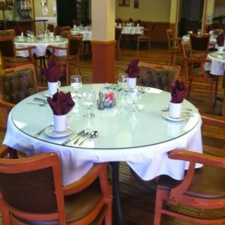A formally set round table in a restaurant with napkins, cutlery, and glassware.