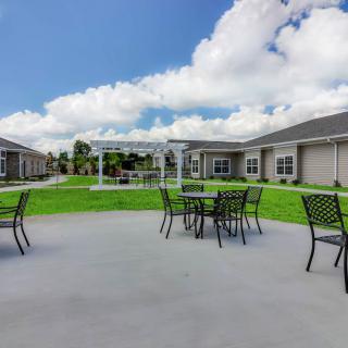 A spacious outdoor patio area with tables and chairs, surrounded by grass and buildings under a partly cloudy sky.
