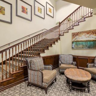 A cozy lobby featuring a wooden staircase, elegant seating area with patterned chairs, and wall artwork.