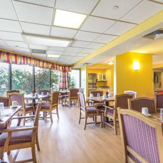 A bright and spacious dining area with tables and chairs, featuring large windows and wooden flooring.