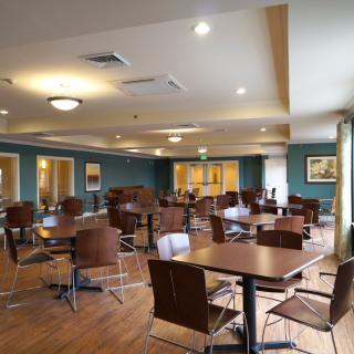 An empty dining area with neatly arranged tables and chairs, featuring warm lighting and wood flooring.