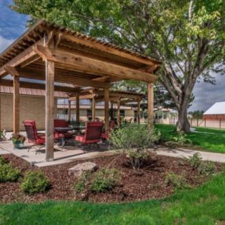 A picturesque outdoor area featuring a wooden pergola with seating, surrounded by a well-maintained garden and trees.