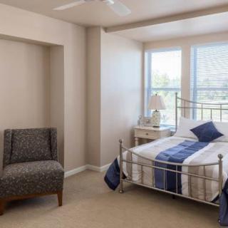 A cozy bedroom with a bed, chair, and large windows.