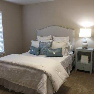 A cozy bedroom with a neatly made bed, featuring multiple pillows and a lit lamp on the nightstand.