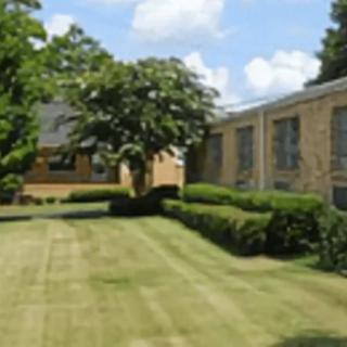 A well-maintained lawn with trees and bushes in front of a brick building under a partly cloudy sky.
