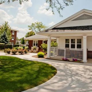 A charming house with a well-maintained lawn and garden, featuring a spacious porch and a paved pathway under a clear sky.