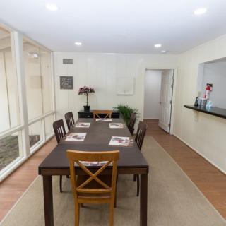 A modern dining room with a long table and chairs, featuring simple decor and warm lighting.