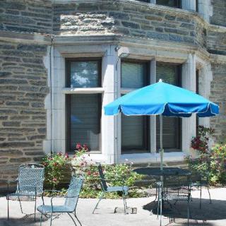A cozy outdoor patio with a blue umbrella, chairs, and a stone building in the background.
