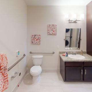 A clean and modern bathroom with accessibility features, including handrails and bright lighting.