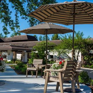 A serene outdoor patio area with chairs and umbrellas surrounded by greenery and flowers.