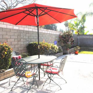 A sunny patio with a red umbrella over a table and chairs.