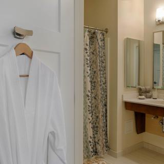 A cozy bathroom with a white robe hanging on the door and a shower in the background.