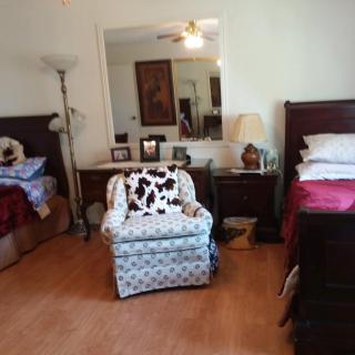 A cozy bedroom with two beds, a patterned armchair, and various decorations.