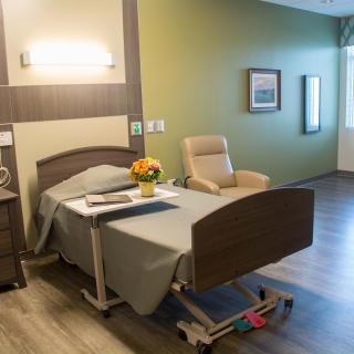 A modern hospital room with a bed, comfortable chair, and decorative flowers.