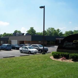 A parking lot in front of a building with several cars and a grassy area on a clear day.