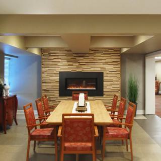 A modern dining room featuring a wooden table with red upholstered chairs, set against a stone wall with an elegant fireplace.