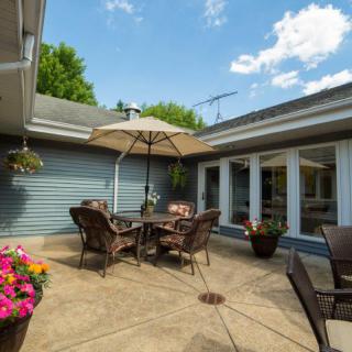 A sunny patio with outdoor furniture and a large umbrella surrounded by flowers.