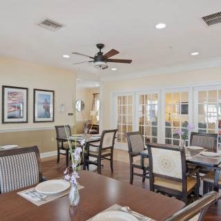 A cozy dining room featuring multiple tables and chairs, decorated with framed pictures and a ceiling fan.