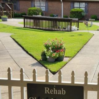 A well-kept garden with a triangular flower bed in front of a rehabilitation center.