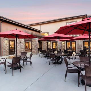 A spacious restaurant patio with tables and chairs under red umbrellas at sunset.