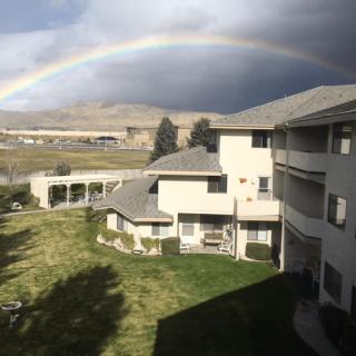 A vibrant rainbow arches over apartment buildings on a cloudy day.
