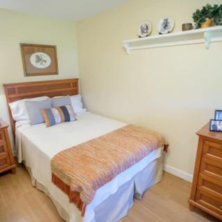 A cozy bedroom with a neatly made bed, wooden nightstands, and decorative items on a wall shelf.
