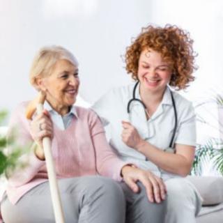 A nurse smiling and providing support to an elderly woman at home.